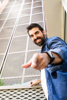 Bearded smiling male leaning on wall while pointing to you with finger