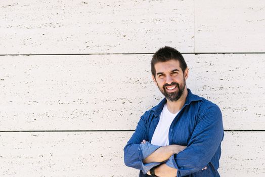 Bearded male leaning on wall with crossed arms while looking camera with a smile