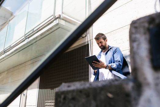 Portrait of a bearded man sitting on steps while using a tablet