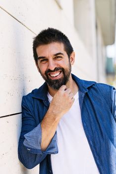 Cheerful bearded male with hand on chin while looking camera