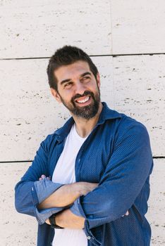 Bearded male leaning on wall with crossed arms while looking away with a smile