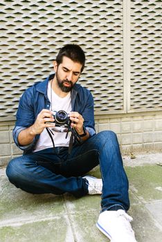 Cheerful bearded traveler man sitting on ground while using checking a camera