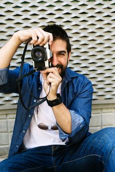 Cheerful bearded traveler man sitting on ground while using checking a camera