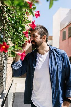 Portrait of bearded male smelling flowers in a city street