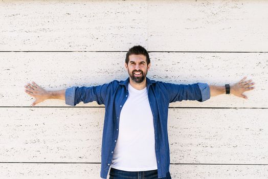 Bearded man leaning on wall with Stretched arms while looking camera with a smile