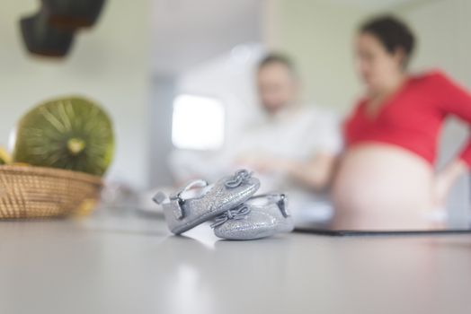 Baby shoes on a kitchen table while expecting couple standing unfocussed in the background