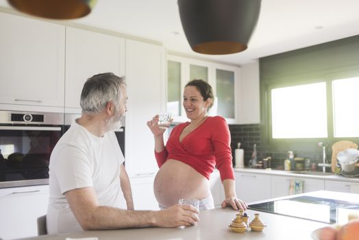 Portrait of smiling laughing white Caucasian couple two people, pregnant woman with husband in the kitchen, lifestyle healthy pregnancy happy life concept