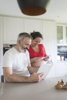 Smiling couple consulting a book at the kitchen.