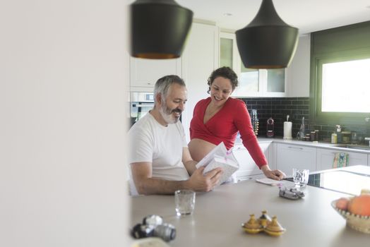 Smiling couple consulting a book at the kitchen.