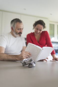 Smiling couple consulting a book at the kitchen.