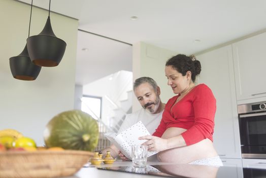 Smiling couple consulting a book at the kitchen.