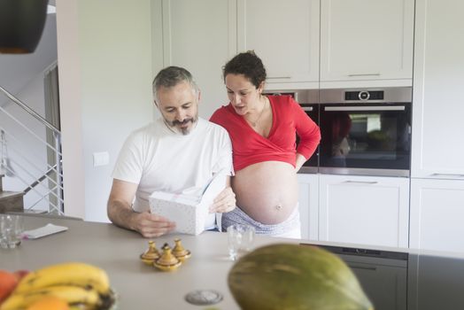 Smiling couple consulting a book at the kitchen.