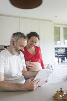 Smiling couple consulting a book at the kitchen.