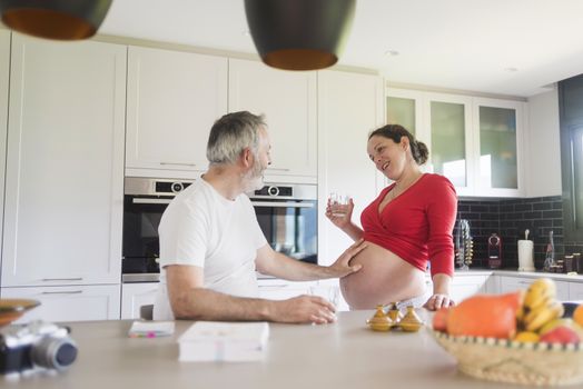 Portrait of smiling laughing white Caucasian couple two people, pregnant woman with husband in the kitchen, lifestyle healthy pregnancy happy life concept