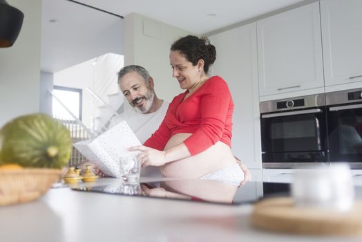 Smiling couple consulting a book at the kitchen.