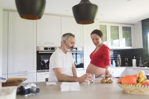 Portrait of smiling laughing white Caucasian couple two people, pregnant woman with husband in the kitchen, lifestyle healthy pregnancy happy life concept