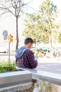 Rear view of a fashion cool urban bearded man with smartphone on city street.