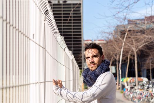 Portrait of relaxed casual man leaning on a metallic fence while looking camera