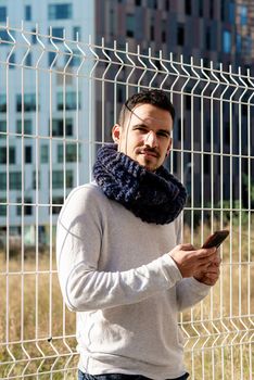 Young bearded man leaning on a metallic fence while using a smartphone