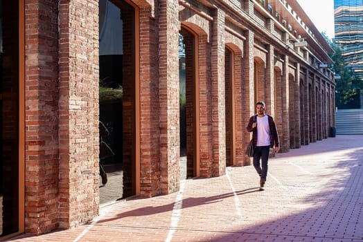 Bearded young male holding shoulder bag while walking in a business district