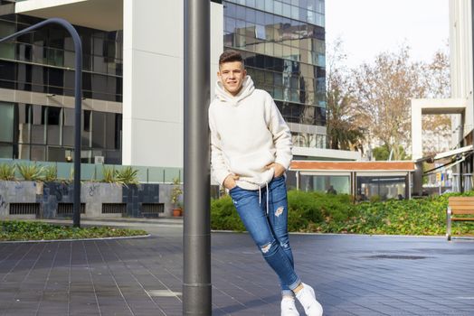 Portrait of young male with hands on pocket leaning on pole outdoors