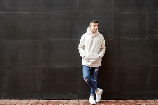 Portrait of young male with hands on pocket leaning on wall outdoors