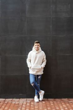 Portrait of young male with hands on pocket leaning on wall outdoors