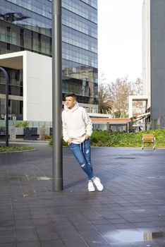 Portrait of young male with hands on pocket leaning on pole outdoors