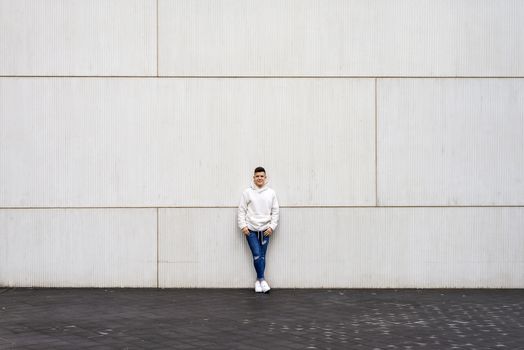 Portrait of young male with hands on pocket leaning on wall outdoors