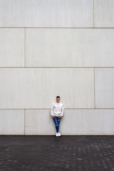 Portrait of young male with hands on pocket leaning on wall outdoors