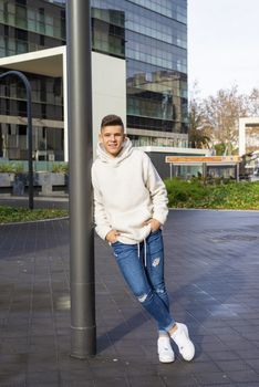 Portrait of young male with hands on pocket leaning on pole outdoors