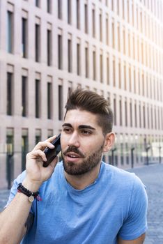 Portrait of cheerful modern businessman speaking by phone and smiling while sitting outdoors in a bench