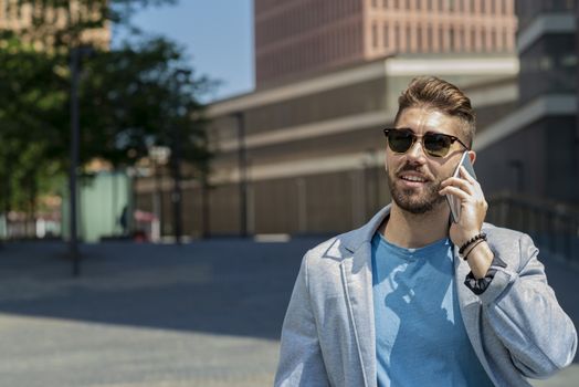 Portrait of cheerful modern businessman speaking by phone and smiling while standing outdoors