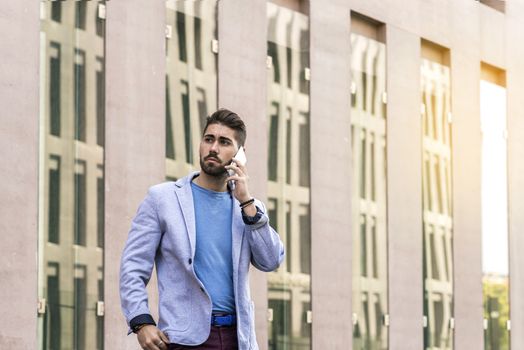 Portrait of cheerful modern businessman speaking by phone and smiling while standing outdoors