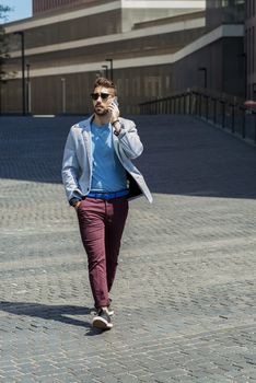 Portrait of cheerful modern businessman speaking by phone and smiling while walking outdoors