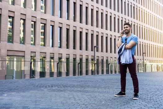 Portrait of cheerful modern businessman speaking by phone and smiling while standing outdoors