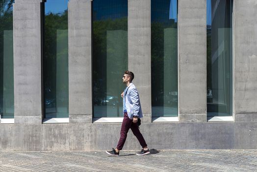 Young businessman walking next to office buildings while holding a shoulder bag outdoors