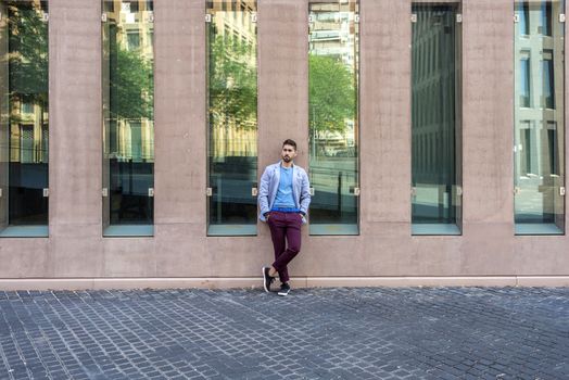 Young bearded man, model of fashion, in urban background wearing casual clothes while leaning on a office building wall