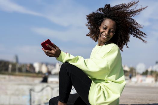 Afro american woman sitting on shore using a mobile phone in a sunny day