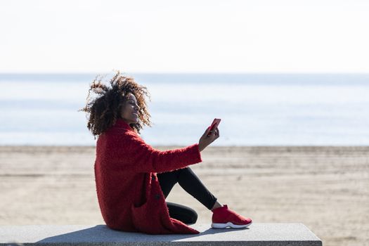 Afro american woman sitting on shore using a mobile phone in a sunny day