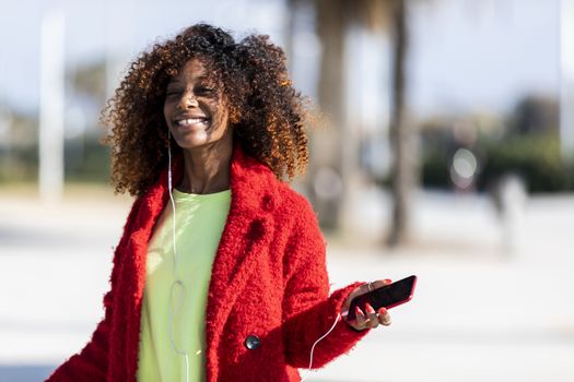 Young afro american woman laughing while dancing outdoors with red jacket