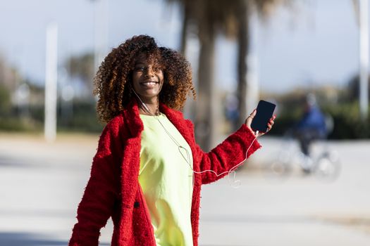 Young afro american woman laughing while dancing outdoors with red jacket