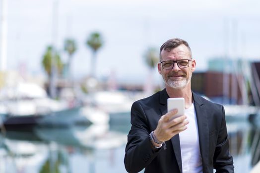 Mature man using cell phone while standing outdoors against harbor