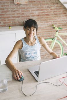 Smiling woman with laptop working at home while looking camera