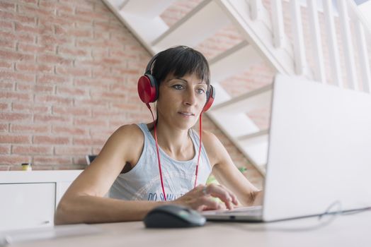 Woman with laptop working at home while listening music by headphones