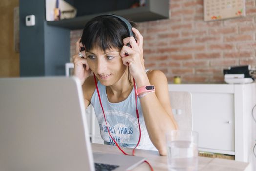 Woman with laptop working at home while listening music by headphones