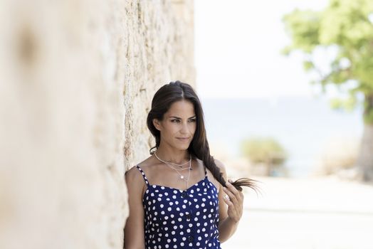 Beautiful smiling woman in blue dress leaning on wall while looking away