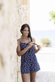 Beautiful smiling woman in blue dress leaning on wall while looking away