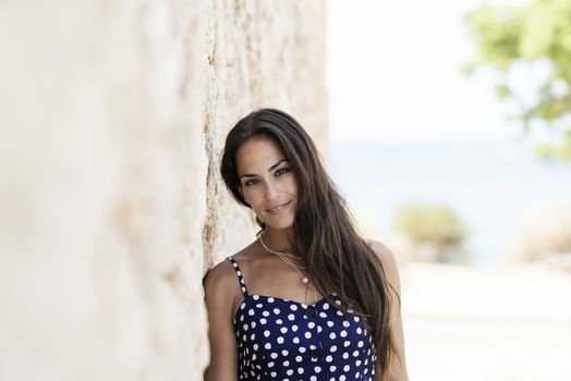 Beautiful smiling woman in blue dress leaning on wall while looking camera