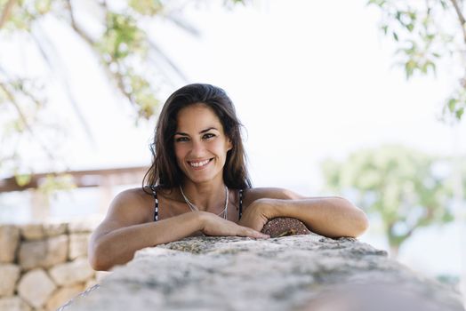 Beautiful smiling woman in blue dress leaning on wall while looking camera
